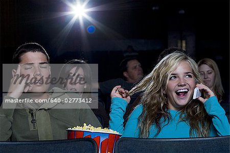 Mädchen reden auf Handy im Kino mit genervt boy