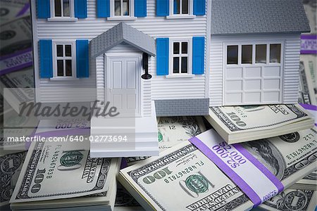 Toy house on pile of one hundred dollar bills