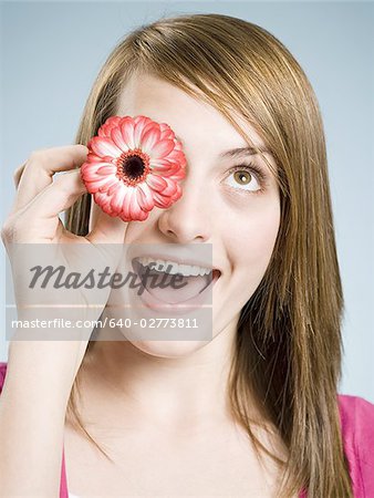 Close-up of woman smiling holding flower up to her eye