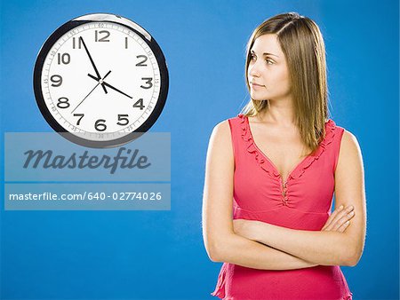 Woman with arms crossed looking at wall clock attached to plumbing pipes