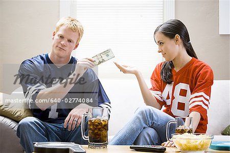 Man and woman in football jerseys handing woman money