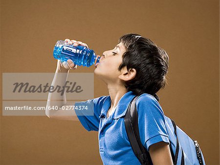 Profile of boy with backpack drinking beverage from plastic bottle