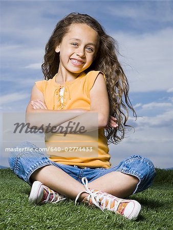 Girl sitting cross legged on grass outdoors with arms crossed smiling