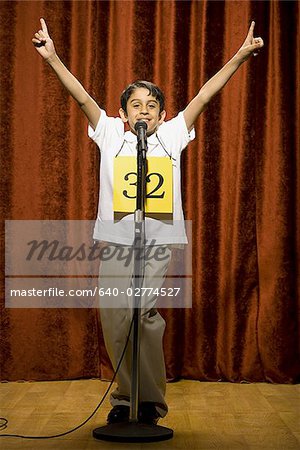 Boy contestant standing at microphone waving and smiling