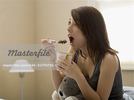 Woman eating chocolate ice cream in bed with stuffed animal
