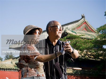 Mature couple dancing outdoors with blue sky and pagoda in background