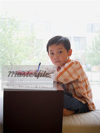 Boy sitting with workbook in front of large window smiling