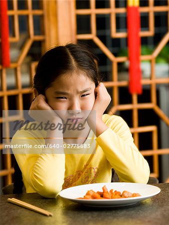 Fille assise à table, assiette de nourriture en regardant avec dégoût