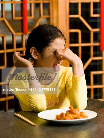 Fille assise à table, assiette de nourriture en regardant avec dégoût