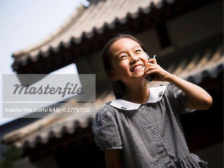 Jeune fille debout à l'extérieur avec le téléphone cellulaire en face de la pagode souriant