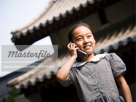 Jeune fille debout à l'extérieur avec le téléphone cellulaire en face de la pagode souriant