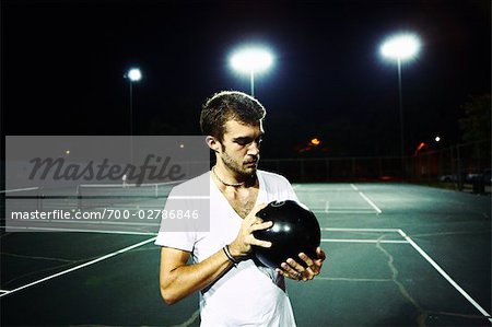 Homme debout sur le Court de Tennis, tenant la boule de Bowling