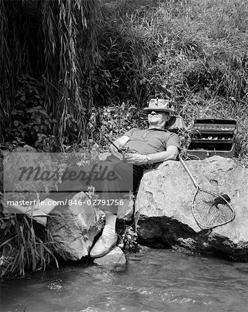 1950s LAZY FISHERMAN LYING BACK ON ROCK WITH HAT PULLED OVER EYES FISHING IN CREEK
