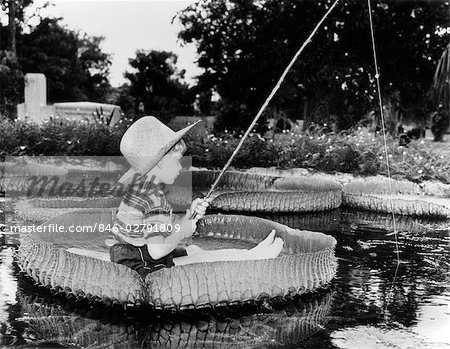 JEUNE GARÇON FLOTTANT SUR LILLY PAD DE PÊCHE EN ÉTANG