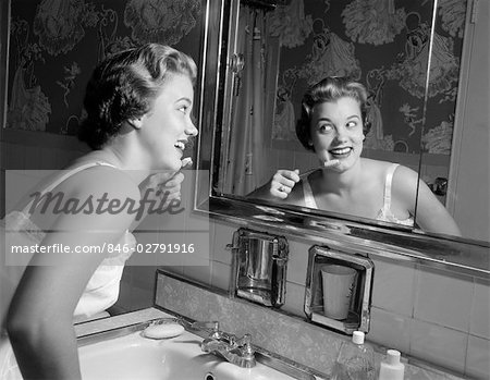 1950s SMILING WOMAN LOOKING INTO BATHROOM MIRROR BRUSHING TEETH