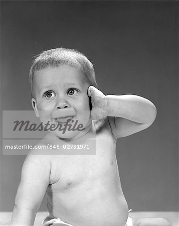 1960s BIG EYED BABY WITH MOUTH OPEN AND TONGUE SHOWING HOLDING 1 ARM UP WITH HIS HAND AGAINST HIS EAR