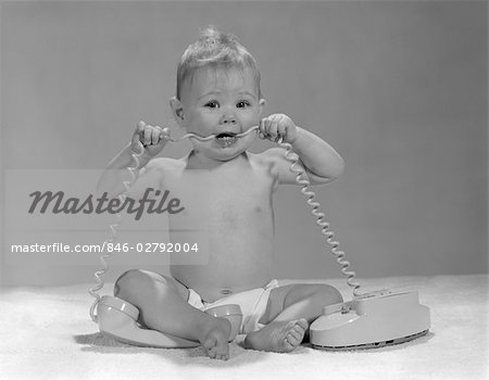 1960s FULL FIGURE BABY SITTING UP LOOK AT CAMERA CHEWING ON TELEPHONE CORD IN MOUTH FUNNY CUTE