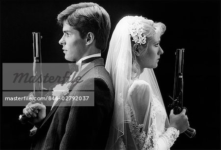 1980s BRIDE AND GROOM BACK TO BACK HOLDING DUELING PISTOLS