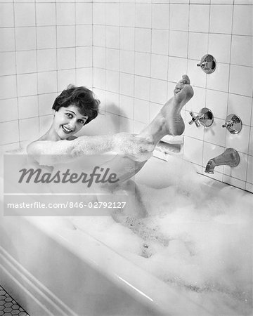 1950s SEXY SMILING WOMAN TAKING A SOAP SUDS BUBBLE BATH IN TUB LOOKING AT CAMERA