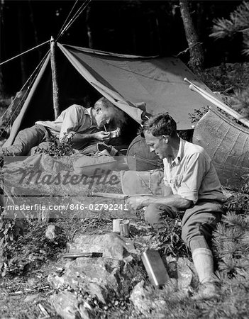 1920s TWO MEN AT PRIMITIVE CAMPSITE ONE MAN IN A FRAME TENT LIGHTING CIGARETTE