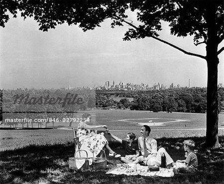 ANNÉES 1940 FAMILLE PIQUE-NIQUER SOUS UN ARBRE DANS LE PARC FAIRMONT AVEC SKYLINE DE PHILADELPHIA PA SUR HORIZON