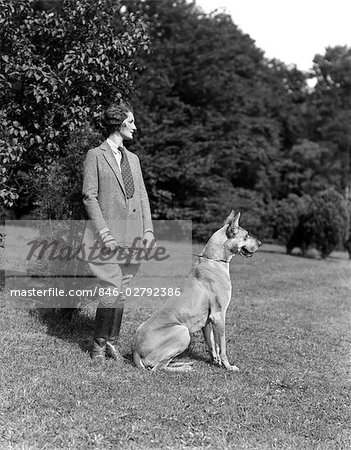 1940s WOMAN WEARING TWEED RIDING SUIT BOOTS STANDING WITH GREAT DANE PROFILE OUTDOOR