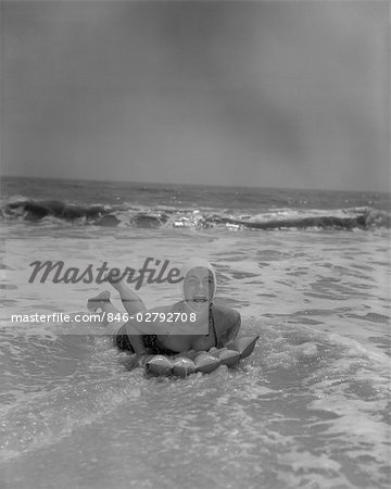 ANNÉES 1950 FEMME RIANT SUR RADEAU GONFLÉ EN SURF