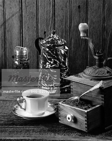 CUP OF COFFEE SITTING NEXT TO AN ANTIQUE GRINDER & A JAR OF BEANS & A COFFEE POT