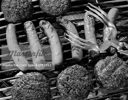 1950s CLOSE-UP OF GRILL FILLED WITH HOT DOGS & HAMBURGERS & TONGS REACHING DOWN TO TURN THEM OVER