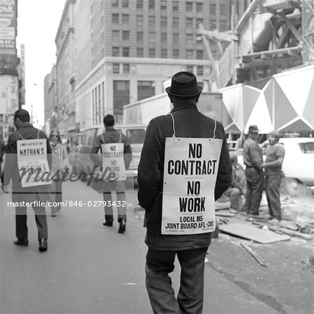 VUE ARRIÈRE DES ANNÉES 1970 DE L'HOMME SE PROMENANT DANS TROTTOIR NE PORTER AUCUN CONTRAT, AUCUN SIGNE DE TRAVAIL AVEC LES AUTRE PIQUETEURS EN ARRIÈRE-PLAN