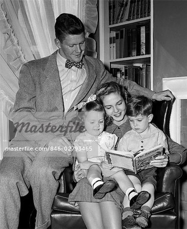 1940s WOMAN  MOTHER IN ARMCHAIR READING TO BOY SON GIRL DAUGHTER WITH PROUD MAN FATHER WATCHING