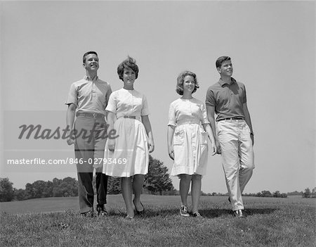 ANNÉES 1960 DEUX COUPLES ADOLESCENTS GARÇONS FILLES PLEINE LONGUEUR MARCHANT DANS LE CHAMP VERS LA CAMÉRA