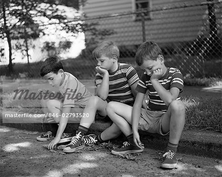 1970s THREE BORED BOYS SITTING ON CURB ALL WEARING STRIPED TEE SHIRTS SHORTS AND SNEAKERS