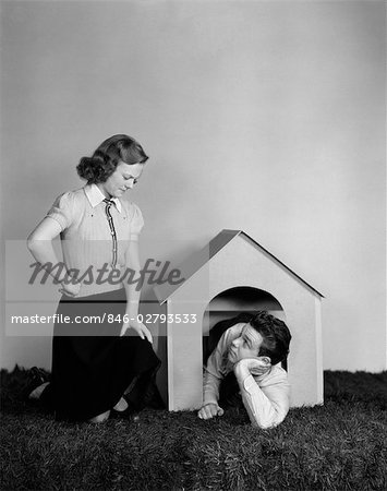 1940s YOUNG TEEN COUPLE ARGUMENT GIRL FROWNING BOY LYING IN DOGHOUSE DOG HOUSE