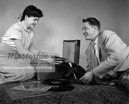 1950s TEEN COUPLE BOY GIRL SITTING FLOOR PLAYING RECORDS ON PORTABLE PHONOGRAPH