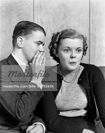 1940s 1930s YOUNG TEENAGE COUPLE BOY WHISPERING INTO GIRL'S EAR GIRL WITH AMAZED SURPRISED EXPRESSION
