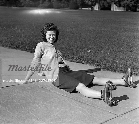 1940s LAUGHING YOUNG WOMAN TEEN GIRL SITTING ON SIDEWALK HAVING FALLEN DOWN ON ROLLER SKATES