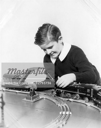 ANNÉES 1930 GARÇON SOURIANT PORTAIT UN CHANDAIL AVEC CHEMISE BLANCHE À COL JOUANT AVEC VOITURE DE GRUE ET LA LOCOMOTIVE DU TRAIN SET DE MODÈLE