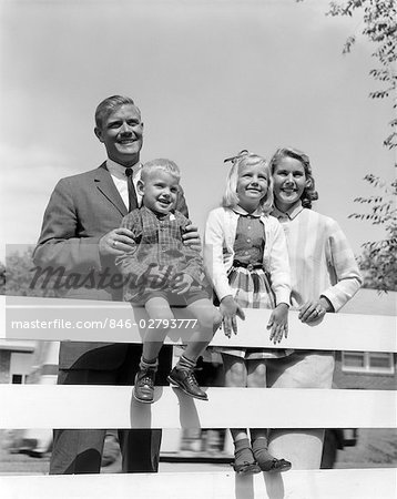 1950s FAMILY PORTRAIT FATHER MAN WOMAN MOTHER GIRL DAUGHTER BOY SON BEHIND BACKYARD FENCE SMILING TOWARDS CAMERA