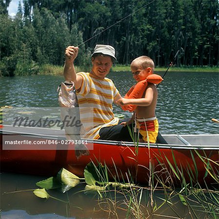 1980s FATHER & SON IN CANOE HOLDING UP CATCH FISH LAKE BOY LIFE PRESERVER FISHING MAN MEN FAMILY ACTIVITY