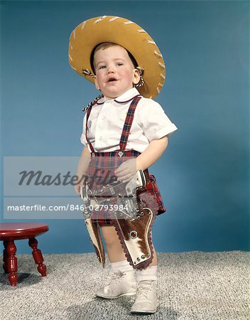 1950s 1960s LITTLE BOY WEARING COWBOY HAT AND TWO SIX GUN CAP PISTOLS HOLSTERS STANDING WITH ATTITUDE