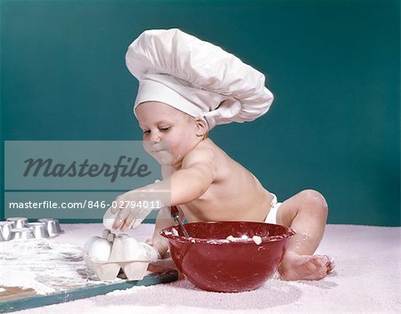 CHAPEAU DE BÉBÉ PORTER DES CHEFS DES ANNÉES 1960 TENANT ENTOURÉ D'ÉQUIPEMENT DE CUISSON DES OEUFS