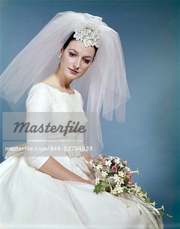 1960s FORMAL PORTRAIT OF BRIDE SITTING HOLDING FLOWER BOUQUET