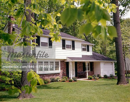 1970s SUBURBAN SPLIT LEVEL HOUSE WITH BLACK SHUTTERS BRICK SIDING AND LANDSCAPED LAWN