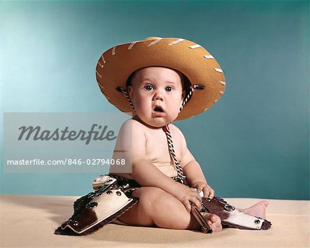 1960s BABY WEARING COWBOY COSTUME WITH FUNNY FACIAL EXPRESSION