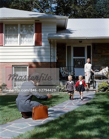 1950s FAMILY WOMAN MOTHER WATCHING MAN FATHER COMING HOME TO SUBURBAN HOUSE KNEELING ARMS EXTENDED TO BOY SON GIRL DAUGHTER RUNNING TO WELCOME HIM HOME