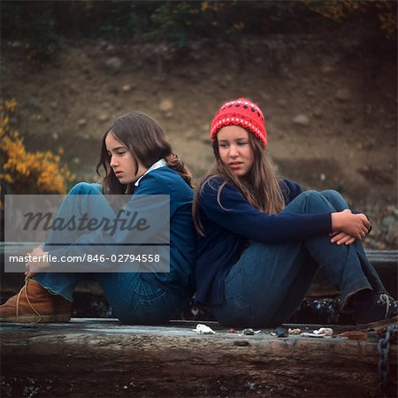 1970s TWO SAD SERIOUS TEENAGE GIRLS SITTING BACK TO BACK OUTSIDE