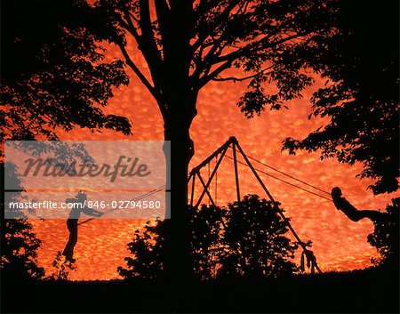 ANNÉES 1970 IMAGE COMPOSITE SILHOUETTÉ ENFANTS JOUANT SUR LA BALANÇOIRE DE GRAND ARBRE AU COUCHER DU SOLEIL