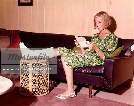 ANNÉES 1960 SOURIANT FEMME JAMBE CASSÉE DANS CAST ON SOFA EN CUIR DE SELLE SÉANCE OUVERTURE ASSURANCE CHECK