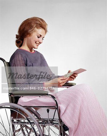 1960s SMILING WOMAN SITTING IN WHEELCHAIR READING INSURANCE CHECK